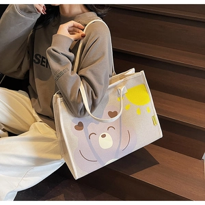 Gros plan d'un sac cabas en toile crème avec motif ours violet sur un escalier en bois