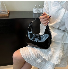 Détail d'un sac demi-lune en cuir verni noir avec finition brillante et fermeture éclair