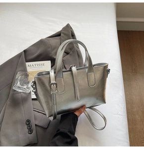 Detail of silver metallic tote bag on white bedding with minimalist accessories