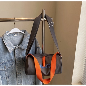 Détail du sac cylindre en toile gris foncé avec bandoulière orange et broderie 1985