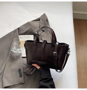 Detail showing glossy dark brown leather texture and metal buckle on a chic tote bag