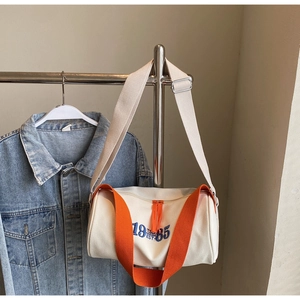 Détail du sac polochon en toile montrant les poignées orange et la broderie 1985 blanche