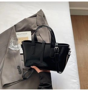 Detail of elegant black glossy faux leather tote bag held against a chic grey blazer