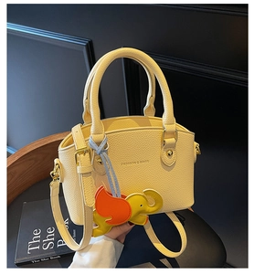 Detail of yellow lychee leather shell bag with elephant charm and gold fashion logo
