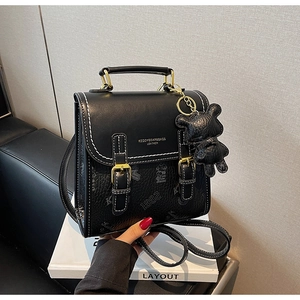 Detail eines schwarzen Kunstleder Rucksacks mit weißen Nähten und Bärenanhänger auf Box