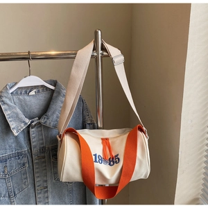 Détail du sac polochon en toile avec poignées orange et broderie 1985 bleue
