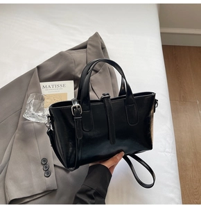 Detailed view of black patent leather tote bag with metallic buckle and shoulder strap