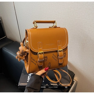 Detail der braunen Ledertasche mit Bärenmustern und weißen Nähten auf einem Luxusbuch