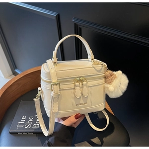 Detail of cream box bag with dual zippers, top handle, and cute plush ball charm