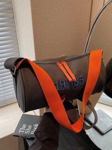 Sac cylindre minimaliste en toile marron foncé avec bandoulière orange et broderie