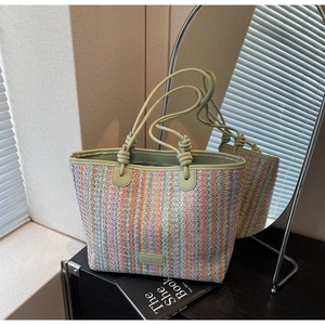 Detail of colorful striped straw tote bag featuring green leather handles and woven texture