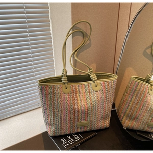 Detail of colorful striped woven tote bag featuring green leather handles and brand plaque