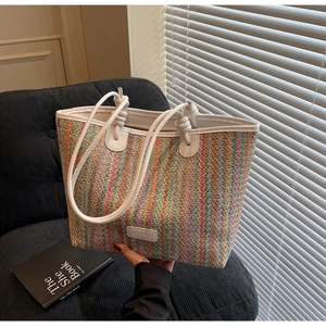 Detail of colorful woven straw tote with white leather trim and brand logo detail