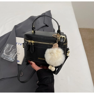 Dettaglio borsa a tracolla nera con zip dorata e ciondolo a pompon bianco soffice