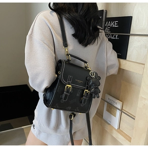 Detail eines schwarzen gemusterten Rucksacks mit Goldschnallen und Bären-Anhänger