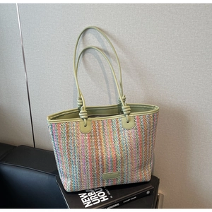 Close-up of multicolored striped woven tote bag with green handles on books