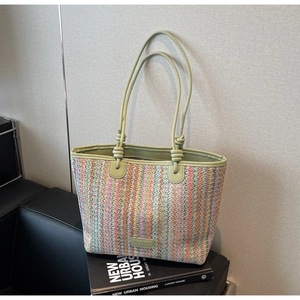 Close-up of colorful straw tote bag with green leather handles and brand logo detail