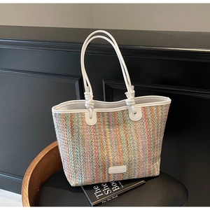 Close-up of a rainbow striped woven tote bag with knotted white straps on a wooden chair