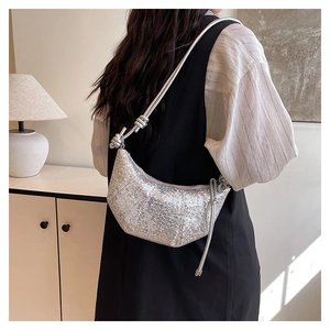 Close-up of a silver sequined crescent bag featuring a knotted shoulder strap and shiny finish