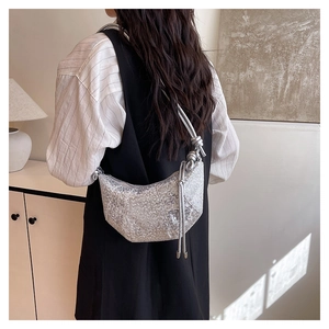 Close-up of a silver sequined crescent crossbody bag with knotted strap detail on a model