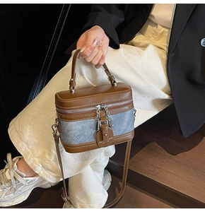 Detail of a brown leather and grey denim box bag with white stitching and metal zippers