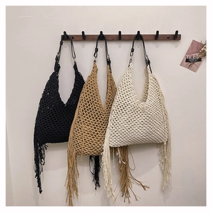 Three handmade woven fringe hobo bags in black, khaki and cream displayed on wall hooks