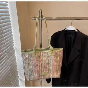 Close-up of colorful striped woven tote bag with green leather straps and logo tag