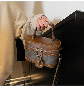 Detail of a retro box-style crossbody bag showing the leather handle and logo tag detail