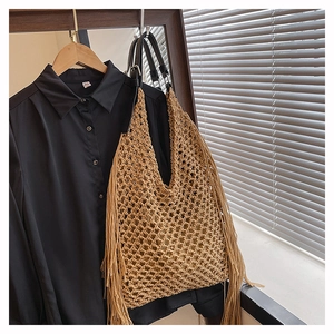 Detail of bohemian hollow hand-woven tassel tote bag with black leather handles and fringe