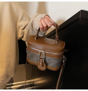 Detail of a brown and grey vanity bag with dual zippers and decorative leather tag