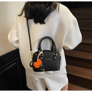 Detail of black pebbled leather shell bag featuring a cute elephant charm on a wooden staircase