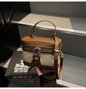 Detail of canvas vanity box bag with brown leather trim and metal chain accents