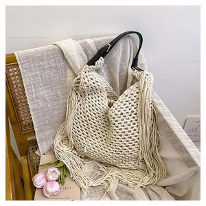 Detail of beige woven tote bag with long tassels on a vintage wooden chair