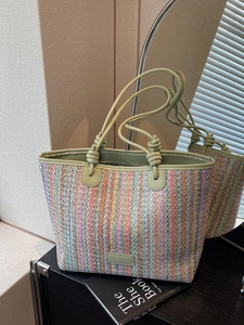 Rainbow striped woven tote bag with green leather handles on a dark table setup