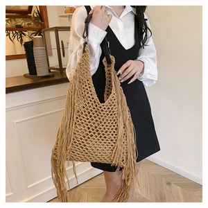Detailed view of beige straw tote bag featuring long fringes and black leather handles