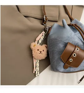 Detail eines Plüschbär-Anhängers mit gewebten Seilen an einer Jeans-Leder-Tasche