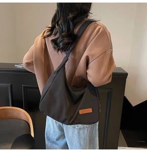 Detail of the minimalist black crescent hobo bag with a brown leather logo patch on nylon
