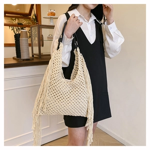 Detail of hand-woven cream tote bag with long tassels and leather handles in a cafe