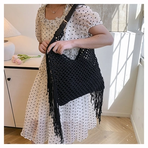 Detail view of black hollow crochet tote bag with long tassels and leather shoulder strap