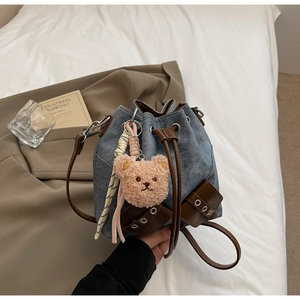 Details der blauen Jeans-Beuteltasche mit braunem Lederbesatz und Plüschbär-Anhänger