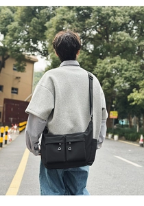 Street style view of a black crossbody dumpling bag with dual utility pockets and wide strap