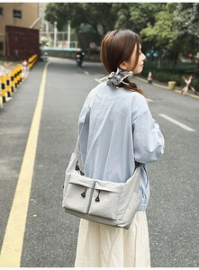Outdoor shot of a light gray waterproof nylon crossbody bag with dual front pockets