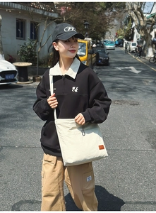 Streetstyle-Ansicht einer cremefarbenen Canvas-Tragetasche mit schwarzer Logo-Stickerei