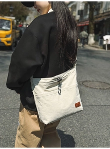 Detail einer cremefarbenen Nylontasche mit Leder-Logo-Patch und Kordelzug-Verschluss