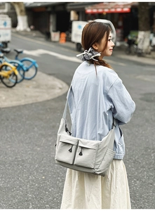 Detail of light gray nylon crossbody bag showing multiple utility pockets and texture