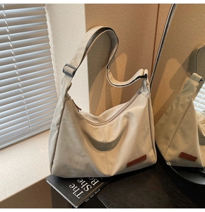Close-up of beige nylon hobo bag with adjustable black strap and brown logo patch