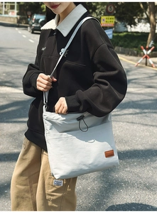 Detailansicht der grauen Nylon-Tasche mit braunem Lederlogo und vorderem Fachdesign