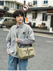 Close-up of khaki nylon messenger bag with functional dual zipper pockets in a street setting