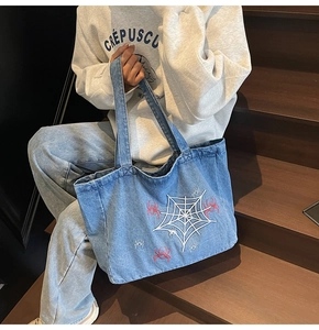 Detail der Spinnennetz-Stickerei und kleiner roter Spinnen auf der hellblauen Denim-Tasche