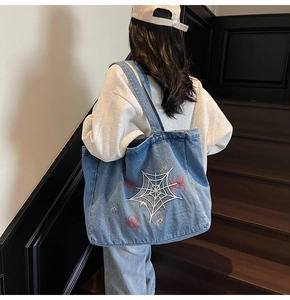 Detailansicht einer blauen Denim-Tragetasche mit Spinnennetz-Stickerei über der Schulter